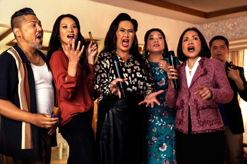 A family group stands singing into karaoke microphones in a living room