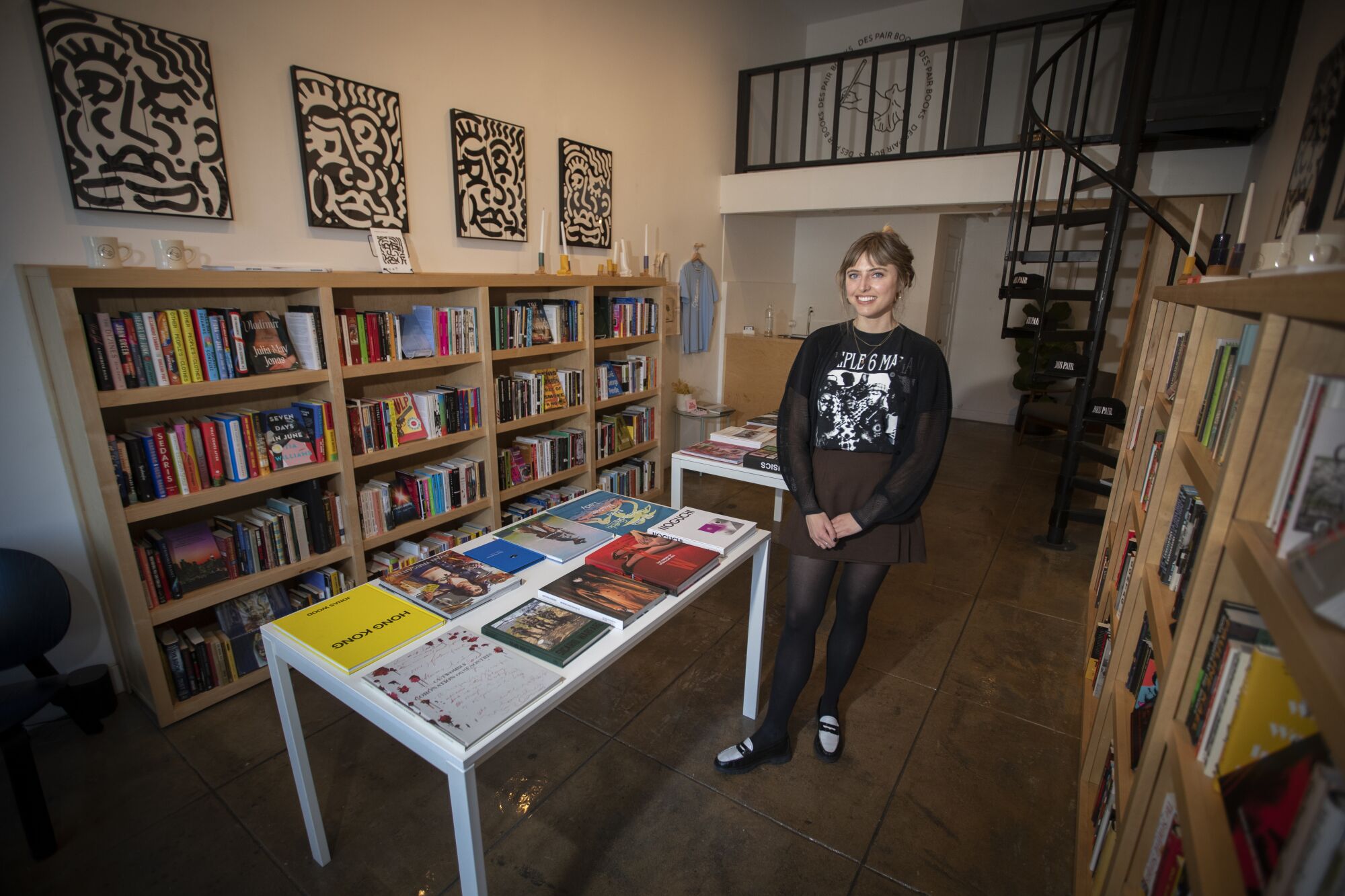 A woman poses in a bookstore with a metal spiral staircase behind her.