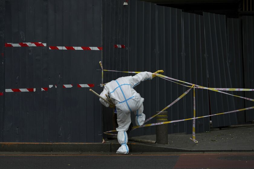 FILE - A worker in protective suit walks through the caution tapes along metal barricades retail shops that has been locked down as part of COVID-19 controls in Beijing, Sunday, June 26, 2022. (AP Photo/Andy Wong, File)
