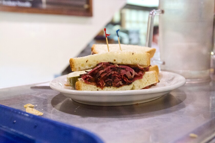 A pastrami sandwich on a white plate that's on a counter