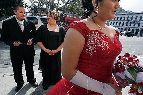 Horacio Arroyo and Maria Soto stand proudly behind their daughter Angelica Arroyo before entering La Placita Church in Los Angeles to celebrate her quinceañera. The traditional Latino celebrations marking a girl's attaining the age of 15 have been gaining in popularity, and their lavishness has been growing.