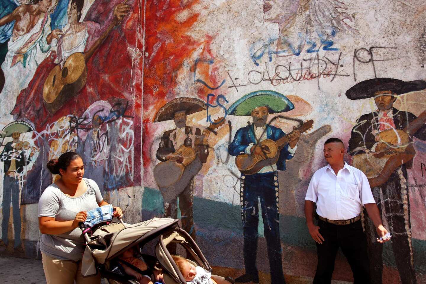 At Mariachi Plaza in Boyle Heights, mariachi Refugio Pena waits next to a defaced mural featuring mariachis to hand out business cards to possible clients. Pena plays with the mariachi group Internacional Varas Nayarit.