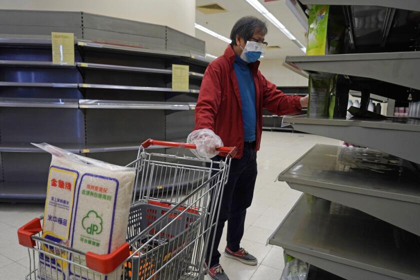 Un hombre portando un cubrebocas y bolsas de plástico como guantes revisa las estanterías vacías en busca de papel higiénico en un supermercado en Hong Kong, el viernes 7 de febrero de 2020.
