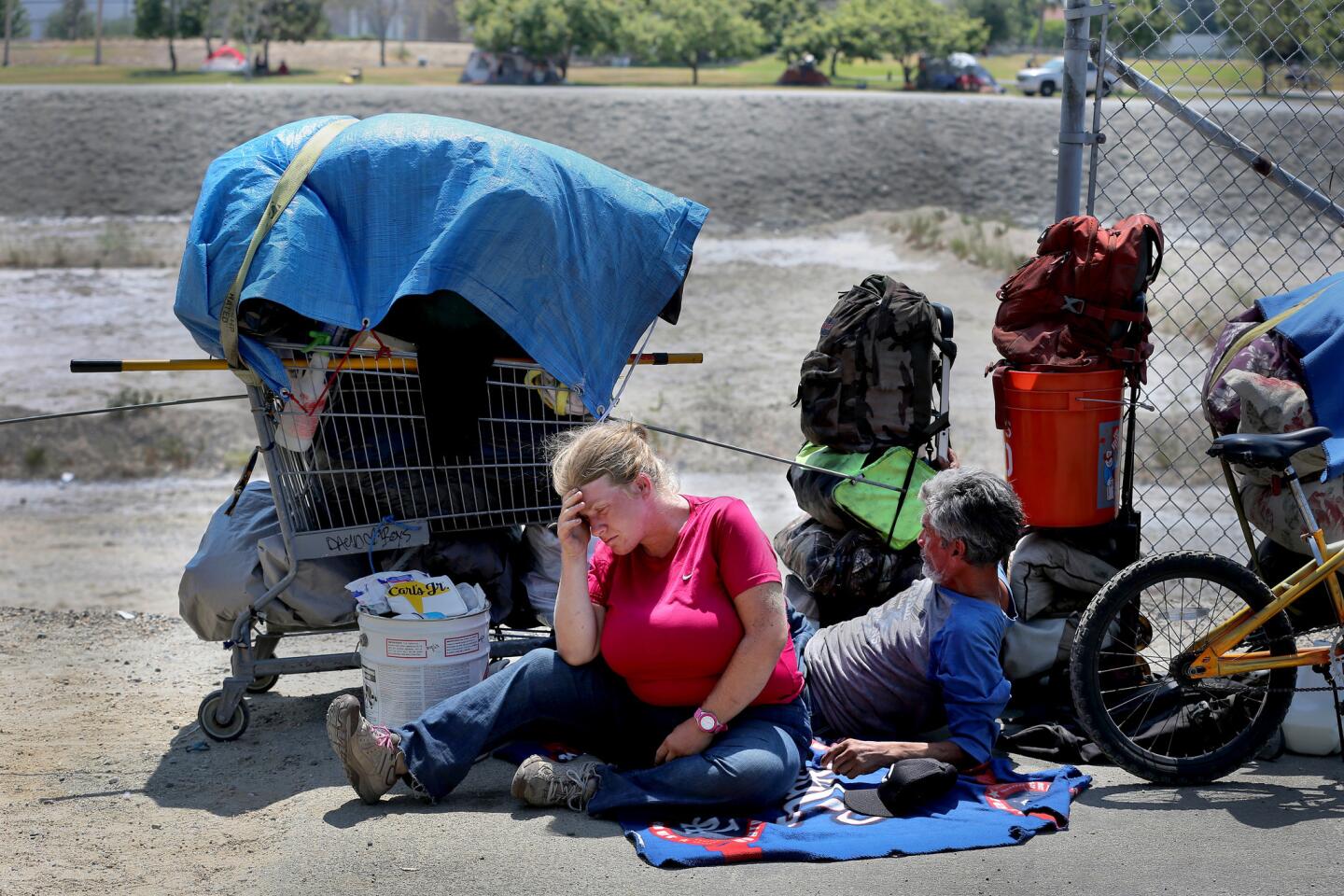 Jennifer Herbst, 31, who is two months pregnant, and fiance John Arispe, 62, are overwhelmed by heat and exhaustion after being evicted Monday from their encampment next to the Honda Center in Anaheim. The couple, who have been homeless for a month, were waiting for homeless outreach volunteers and a moving truck donated by The Rock Anaheim church to move their belongings across the Santa Ana River.