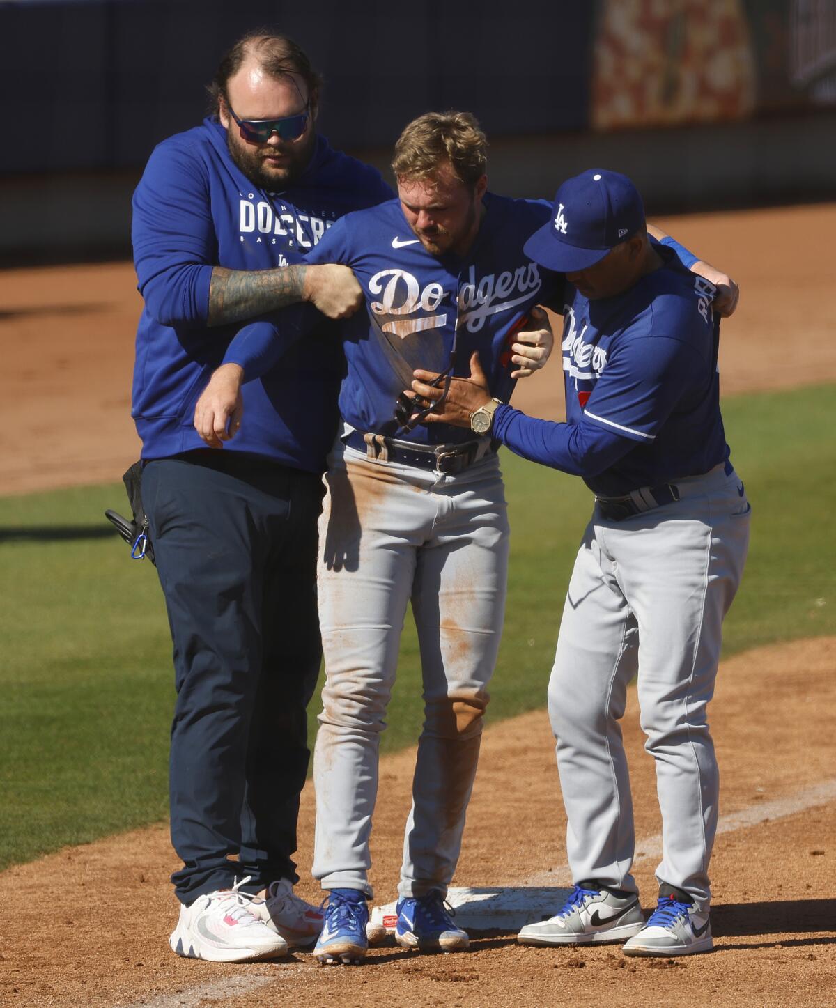 Dodgers' Gavin Lux is helped off the field by a team trainer and manager Dave Roberts.