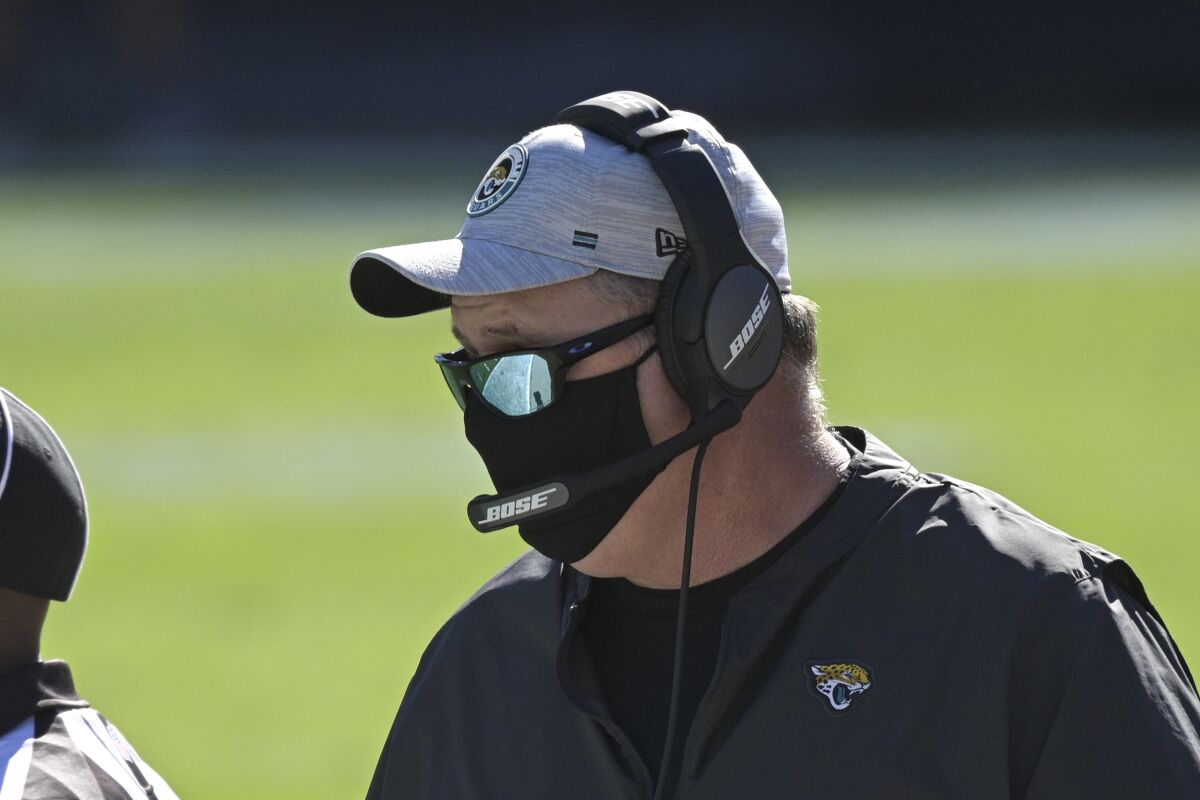 Doug Marrone, in mask and headphones, stands on the sideline.