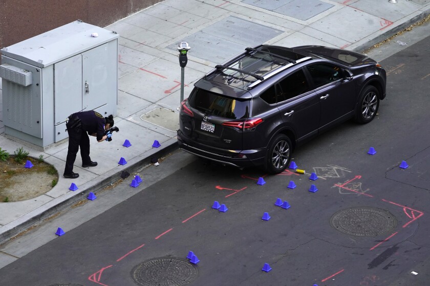 A crime scene investigator photographs blue evidence markers on a street