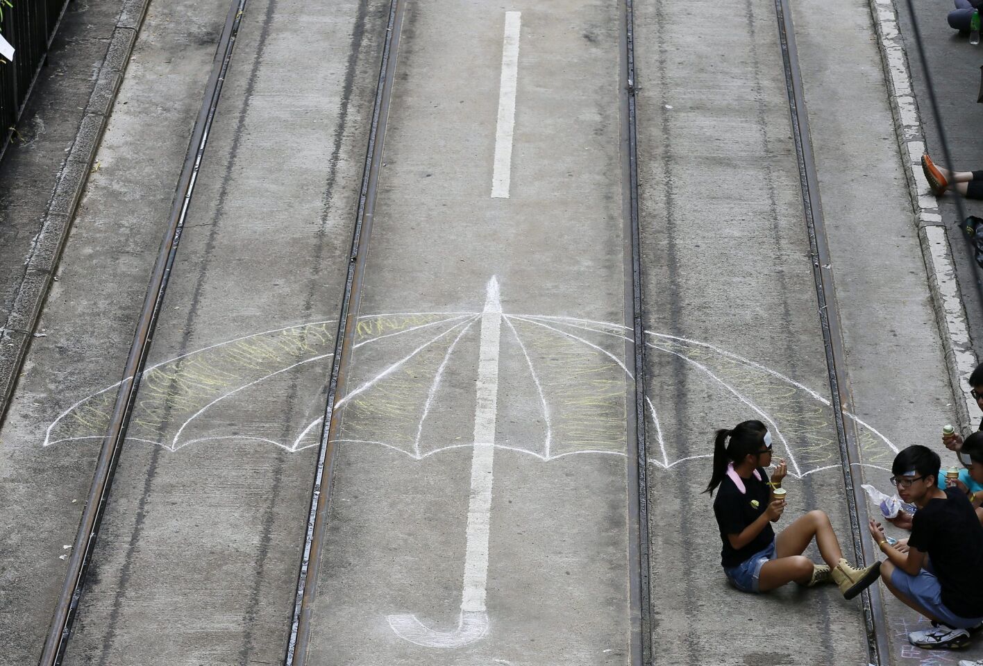 Pro-democracy demonstrators sit on tram tracks with a graffito of an umbrella on the fourth day of the mass civil disobedience campaign in Hong Kong.