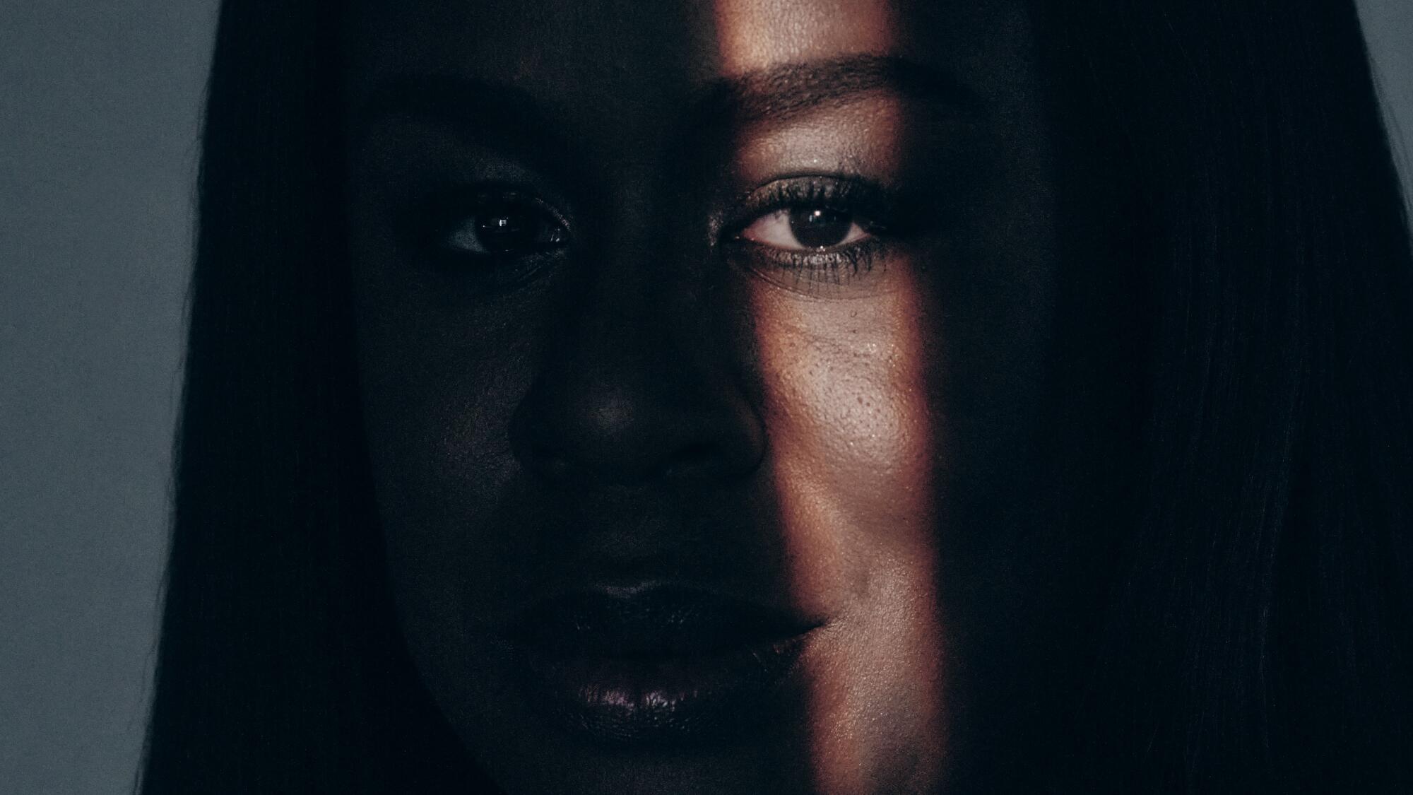 a tight frame of a woman's face with a strip of light illuminating one eye more than the rest