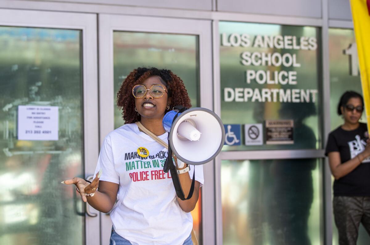 A high school student stands outside office building doors holding a megaphone during a protest.