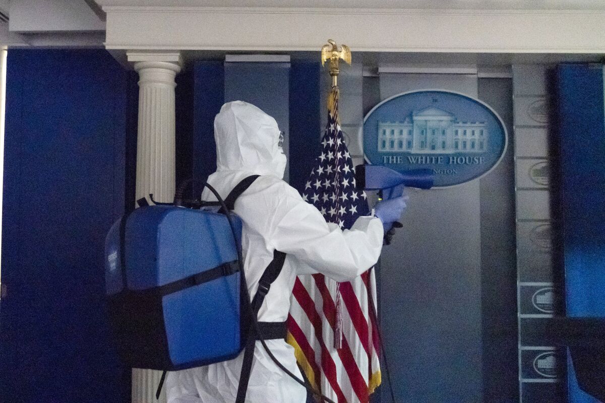 A member of the cleaning staff sprays The James Brady Briefing Room of the White House, Monday, Oct. 5, 2020, in Washington. (AP Photo/Alex Brandon)