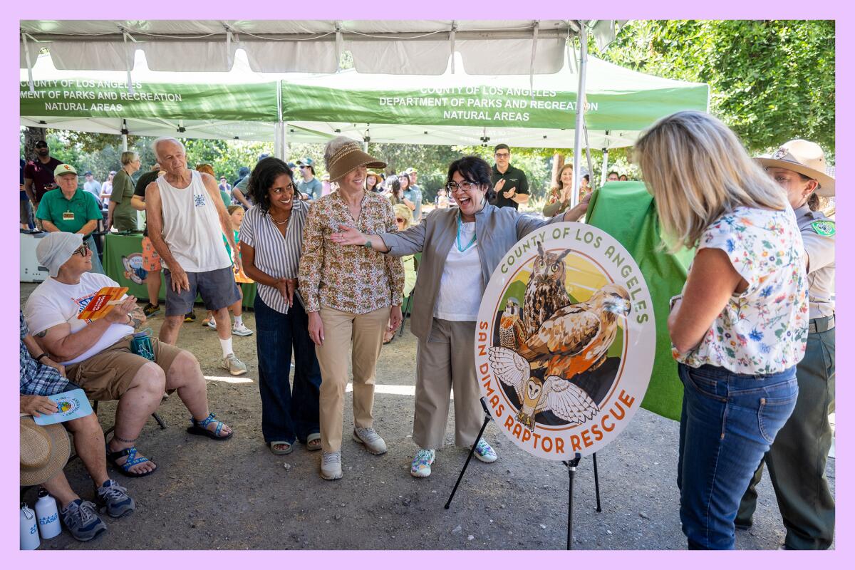 A group of folks celebrates near a circular sign that reads "County of Los Angeles — San Dimas Raptor Rescue."