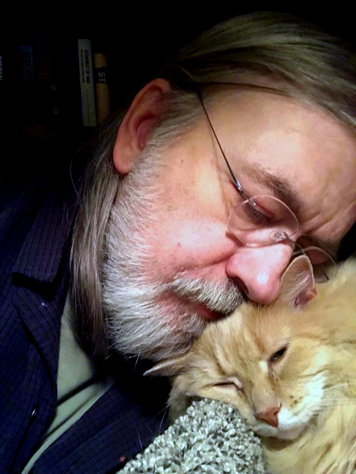 A man snuggles against the top of a cat's head