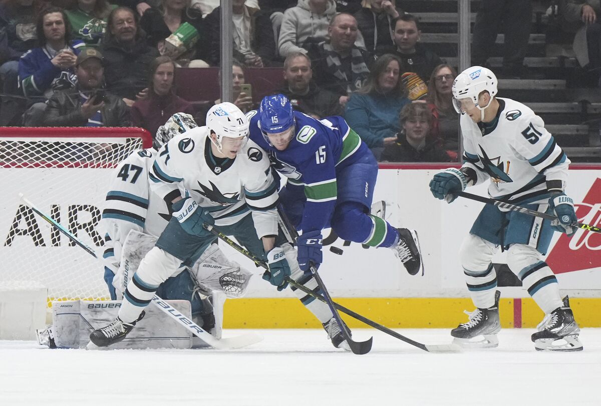 Vancouver Canucks' Sheldon Dries (15) jumps to avoid the puck while being checked by San Jose Sharks' Nikolai Knyzhov (71) in front of goalie James Reimer (47) as Radim Simek (51) watches during the first period of an NHL hockey game in Vancouver, British Columbia, Thursday, March 23, 2023. (Darryl Dyck/The Canadian Press via AP)