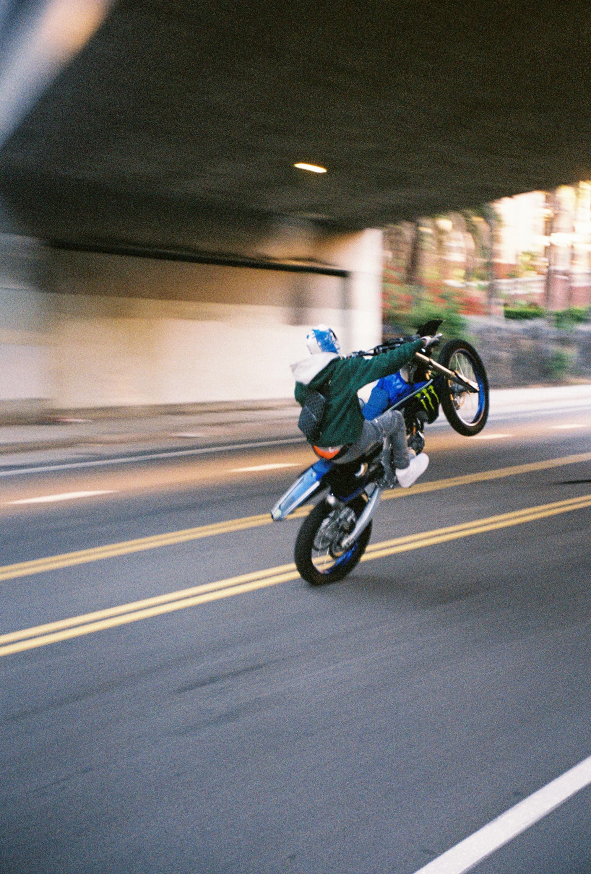 A biker pops a wheelie on a city street going under an underpass.