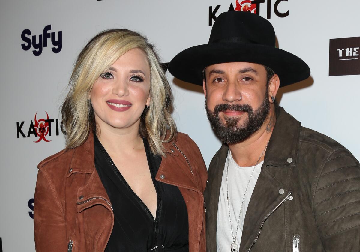 AJ McLean, in a brown jacket and black wide-brim hat, poses with Rochelle McLean, in a light brown jacket and black shirt
