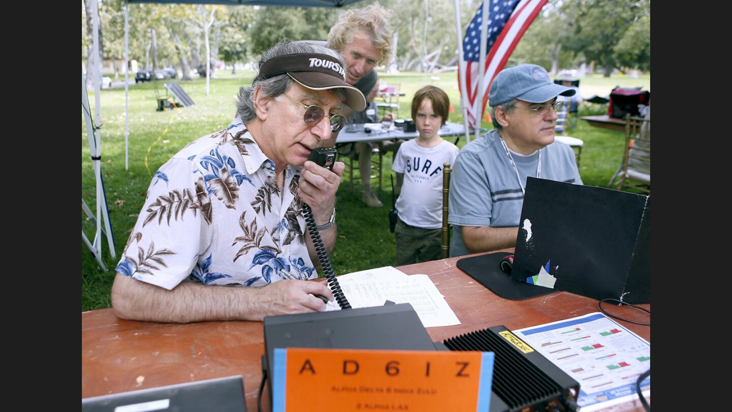 While Ham radio hobbyist Rob Hoegee, rear left, and his six-year old son Henry, rear right, look on, and Crescenta Valley Radio Club team partner Steve Burkholder logs finds at right, Crescenta Valley Radio Club ham radio operator Bob Cesarone, left, gives out the group's call sign Alpha Delta Six India Zulu, AD6IZ, while making contact with another group on national Field Day for ham radio users, at Verdugo Park in Glendale on Saturday, June 24, 2017. Groups throughout the USA and Canada will spend 24 hours trying to make contact with as many different ham radio locations as possible. The Glendale Emergency Auxiliary Radio Service also participated in the event.