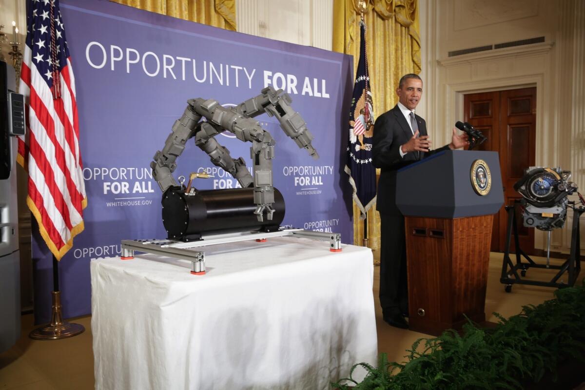 President Obama announces two new manufacturing innovation institutes standing in between a Navy robotic arm and a helicopter engine.