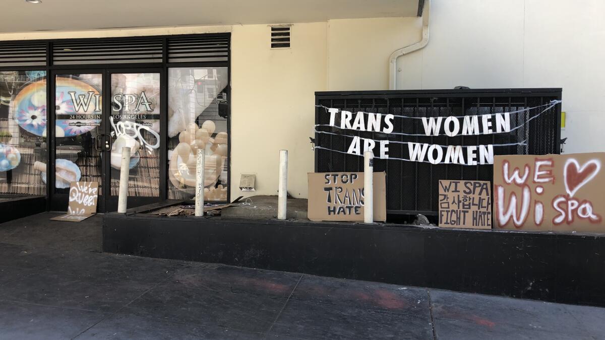 Signs outside a building say 'Trans women are women,' 'Stop trans hate,' 'Wi Spa fight hate,' and 'We heart Wi Spa'