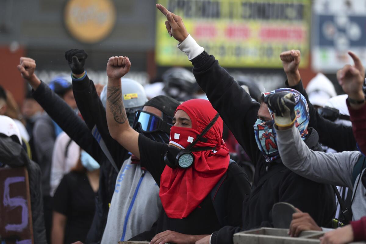 Protesters with faces covered raise their fists.