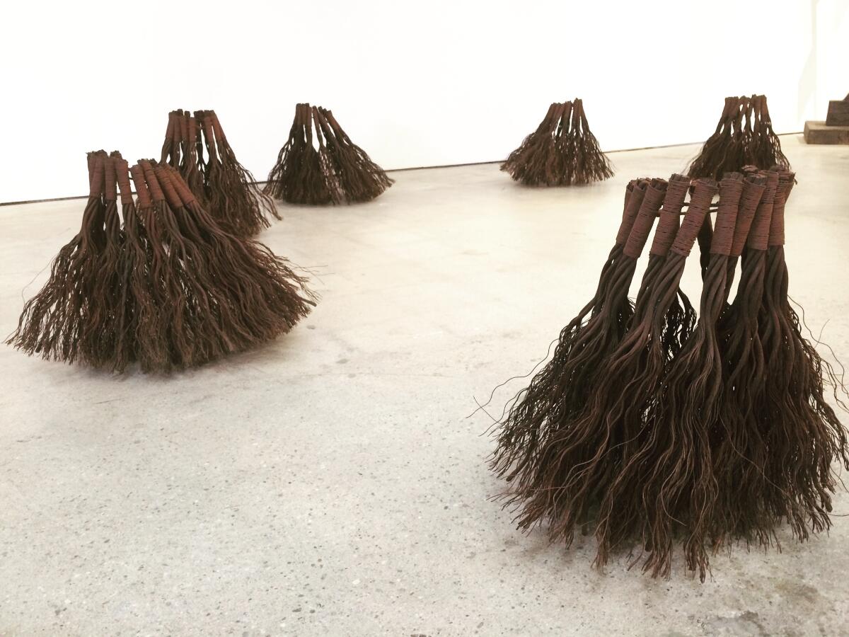 A view of a series of floor sculptures that resemble brushes made out of galvanized wire.