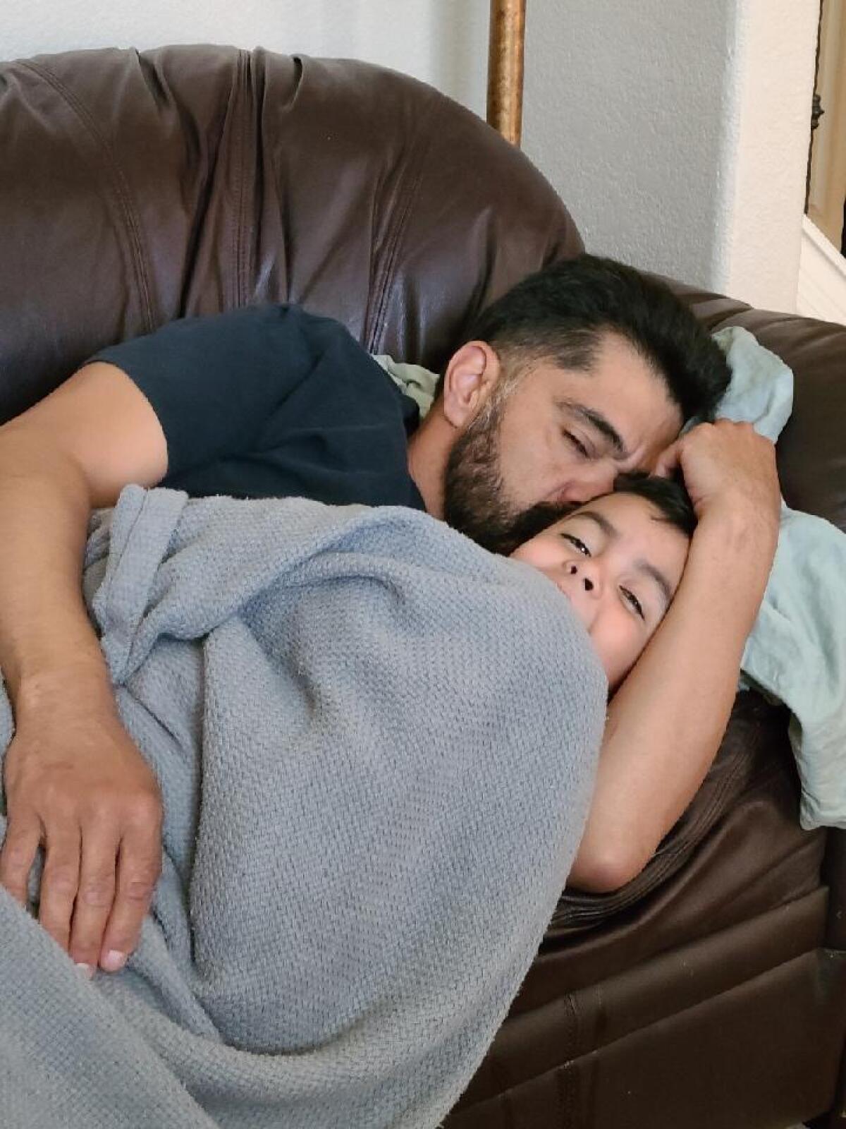 A man and boy nap on a couch