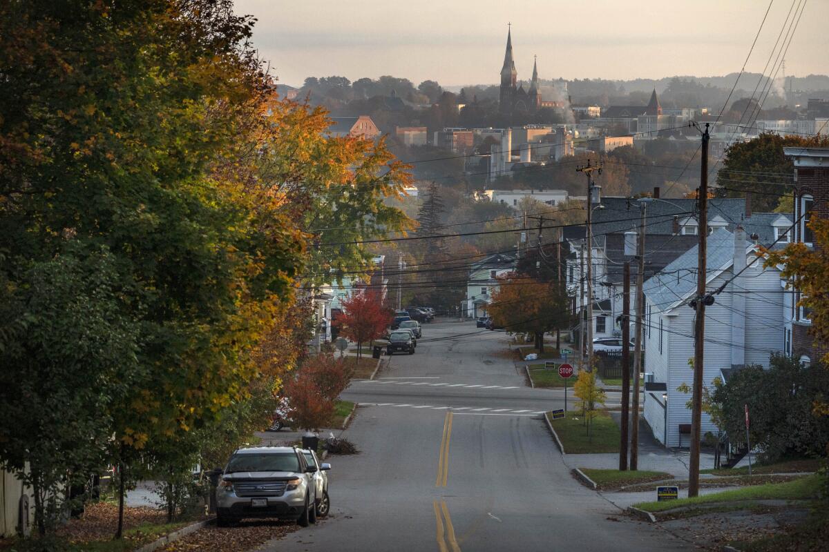 An empty street lined by houses and trees with fall colors, with a church spire in the background.