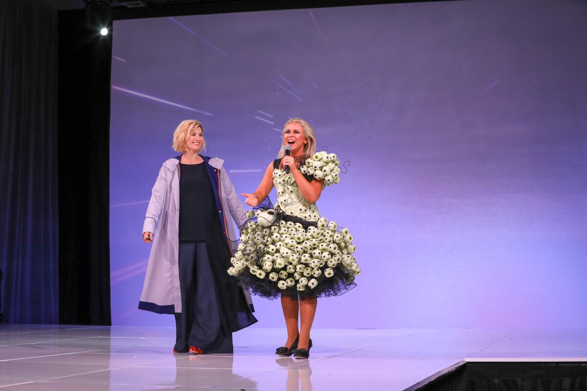 Jodie Whittaker and Ashley Eckstein stand next to one another on stage in front of a purple backdrop.