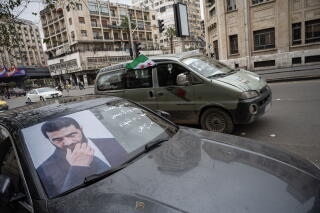A poster of Ahmed al-Sharaa, Syrian politician, is seen on a windshield, as Syrians crowd the streets.