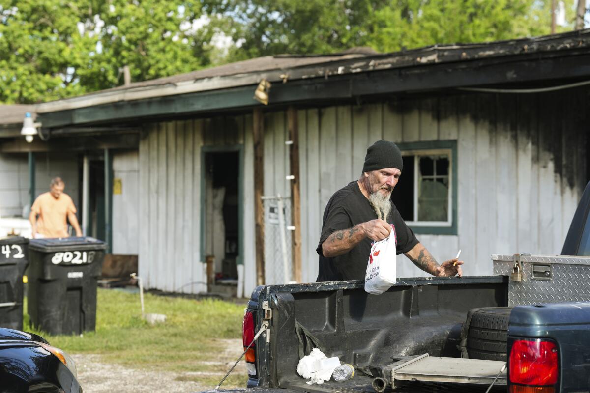 A man walks past a burned out building while another man puts a bag in a truck bed nearby.