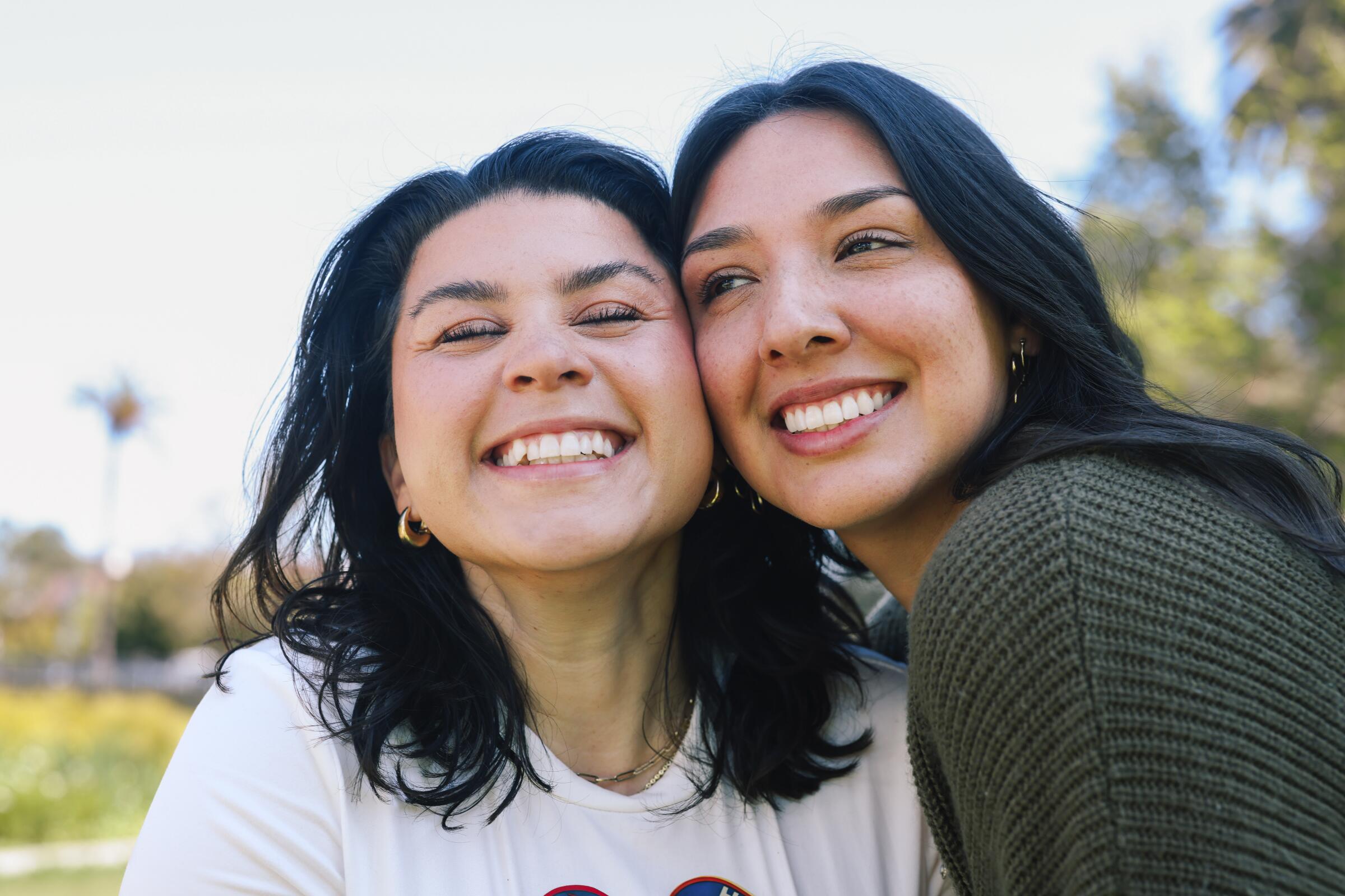 A closeup of two dark-haired women, cheek to cheek, grinning.