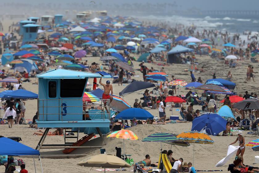HUNTINGTON BEACH, CA - JUNE 15: A life guard keeps watch on the crowd of people on Tuesday, June 15, 2021 in Huntington Beach, CA. Restrictions are lifted at most businesses, and Californians fully vaccinated for COVID-19 can go without masks in most settings. (Gary Coronado / Los Angeles Times)