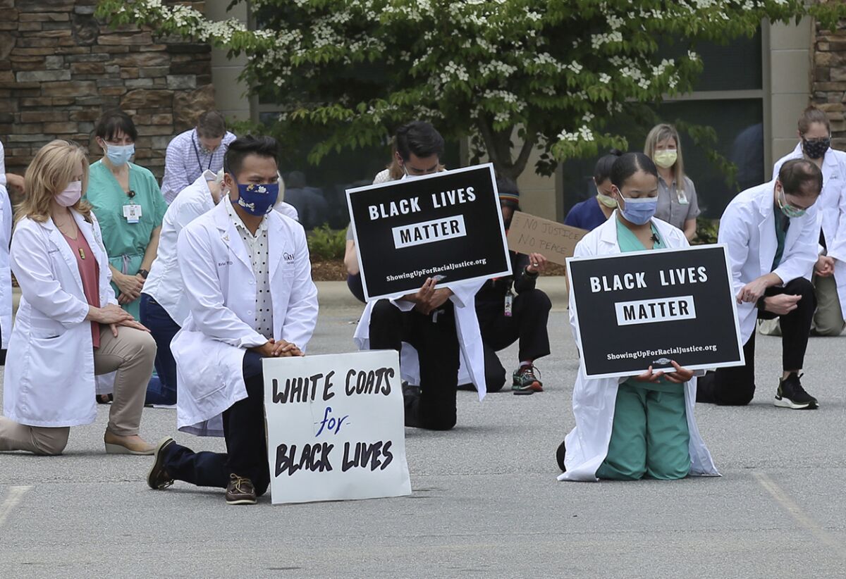 In this June 5, 2020 photo provided by the Mountain Area Health Education Center, physicians, residents and staff from the facility in Asheville, N.C., take a knee to show support for renewed calls for racial justice after the police killing of George Floyd. Government statistics from late January through May 30 suggest an increase in U.S. deaths from chronic diseases compared with historical trends. They include 7,000 excess deaths from hypertension, about 4,000 from diabetes and 3,000 from strokes -- all conditions that disproportionately affect Blacks, although the data don’t include race. (Brenda Benik/MAHEC via AP)