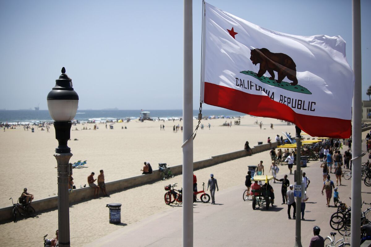 The California flag waves in the breeze as beachgoers enjoy a sunny day near the Huntington Beach Pier.