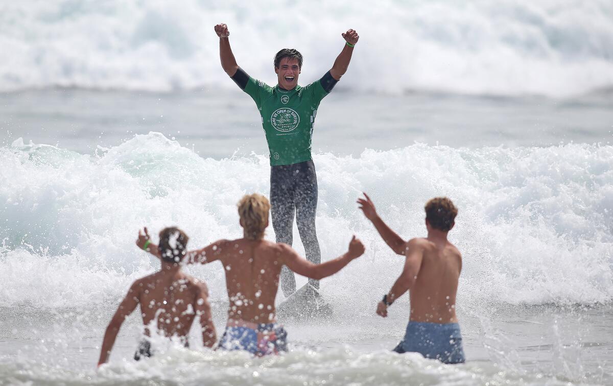 Kade Matson of San Clemente raises his hands in victory as friends rush to congratulate him in the shoreline after he took first in the mens' junior final in the Van's US Open of Surfing at the Huntington Beach Pier on Saturday.