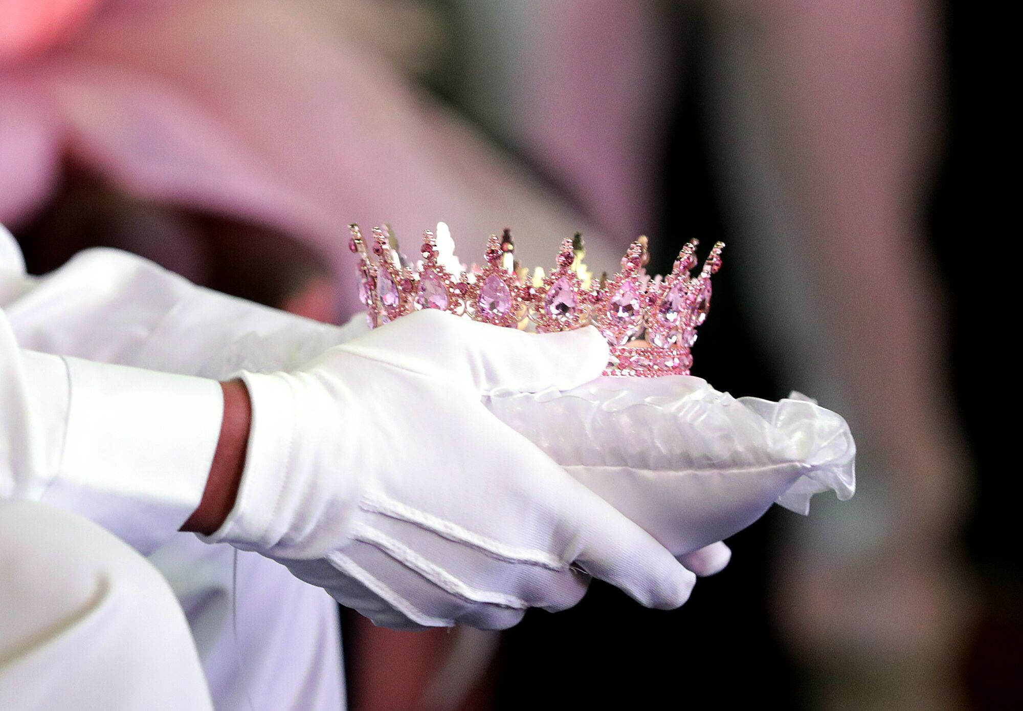 Two hands hold a small pillow with a pink crown on it.