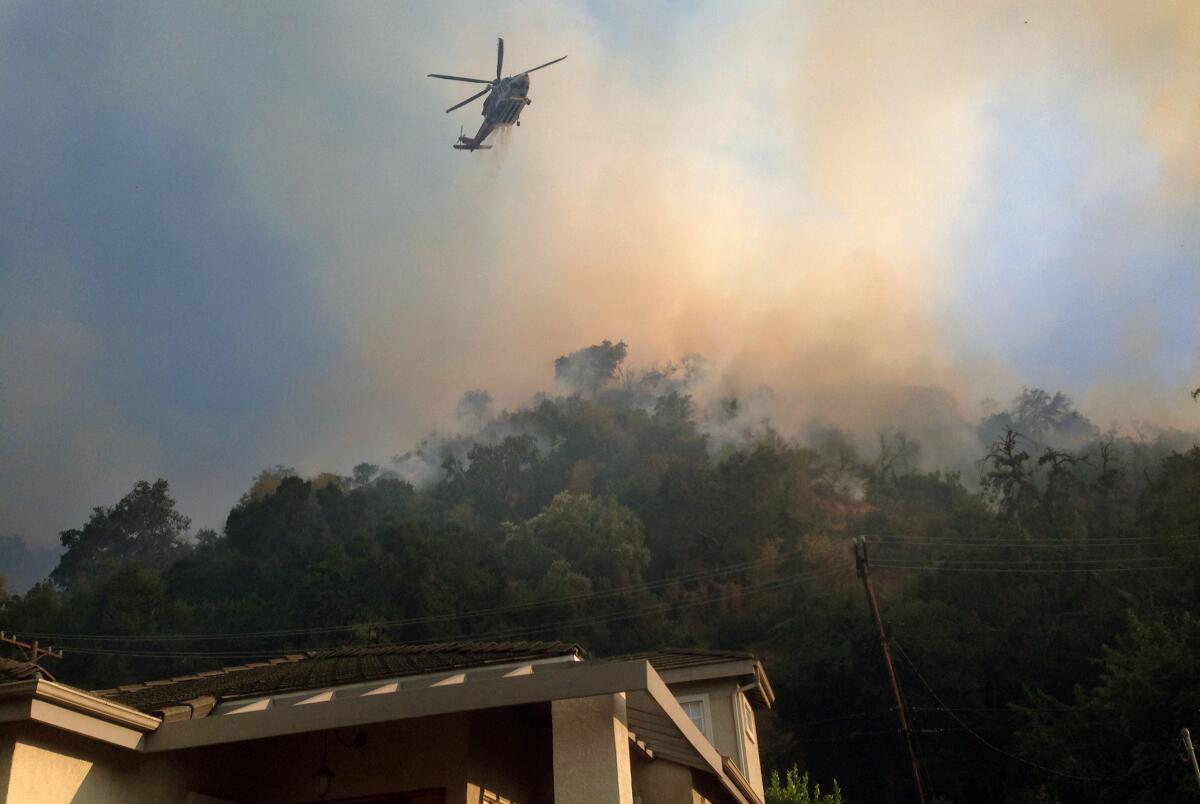 A fire helicopter makes a water drop on a brush fire in the hills behind homes in Glenoaks Canyon on Sunday. The fire started in Eagle Rock, jumped a freeway and made its way into Glendale.