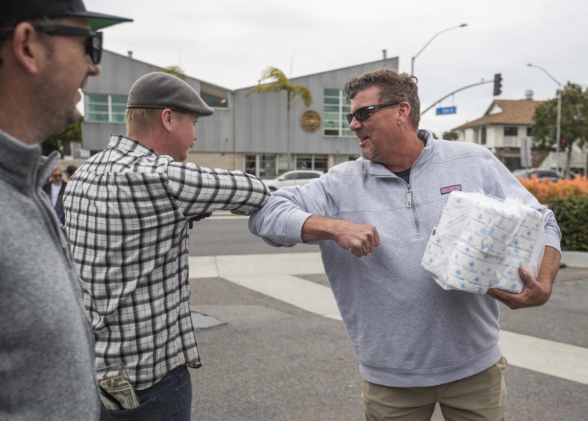 Troy Barton bumps elbows with Josh van Egmond, who bought a bundle of toilet paper outside Malarky's Irish Pub in Newport Beach on Friday.