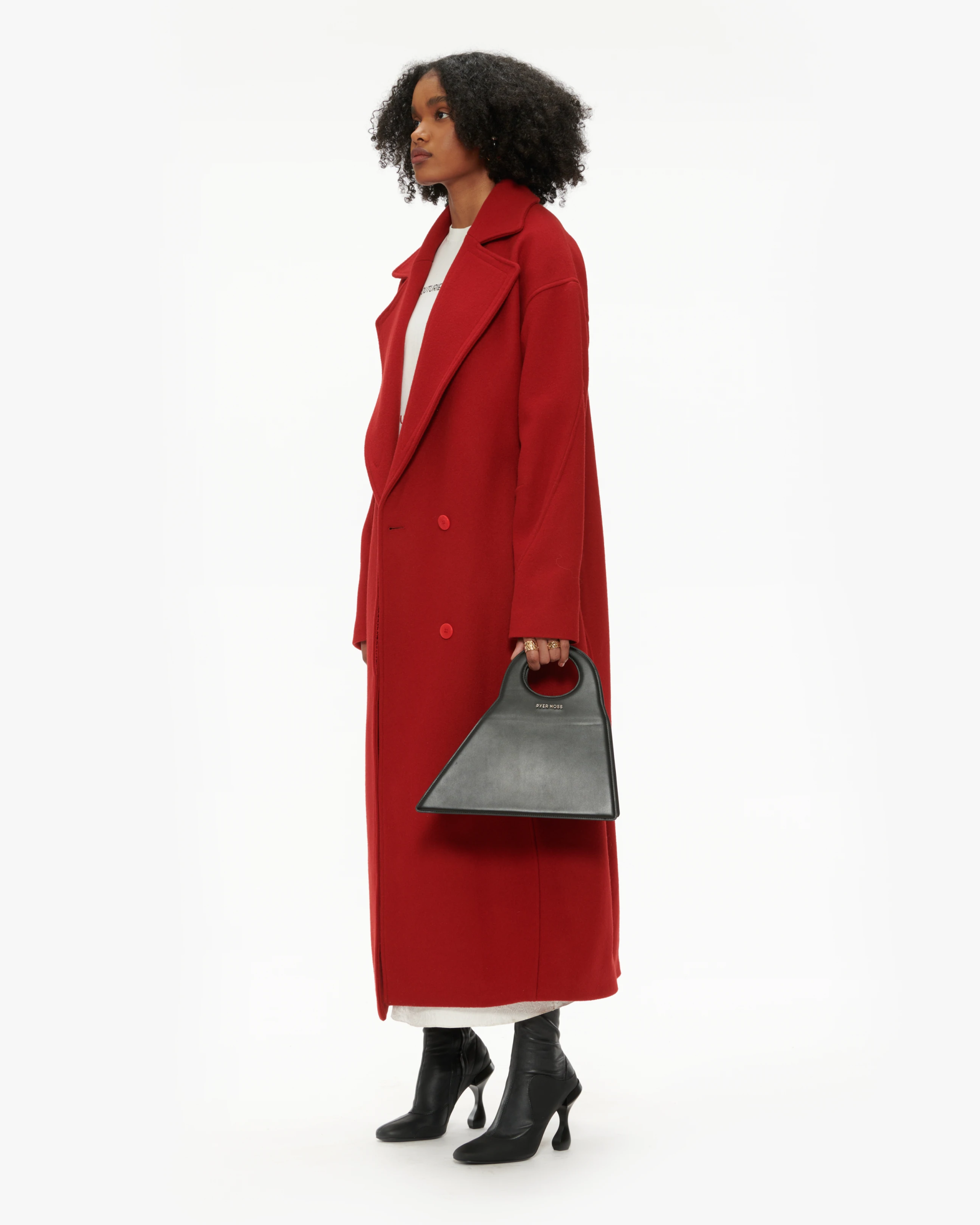 Model in a red overcoat holding a black Pyer Moss handbag