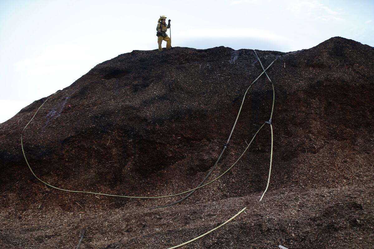 A firefighter stands atop a mountain of wood chips as it smolders a day after the Boles fire swept through a mill in Weed, Calif.
