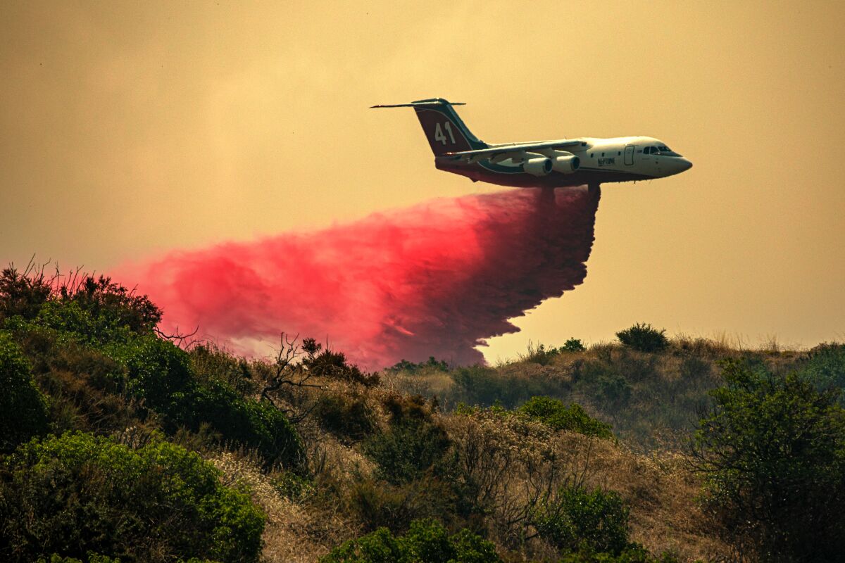 A plane drops a pink substance on a hillside.