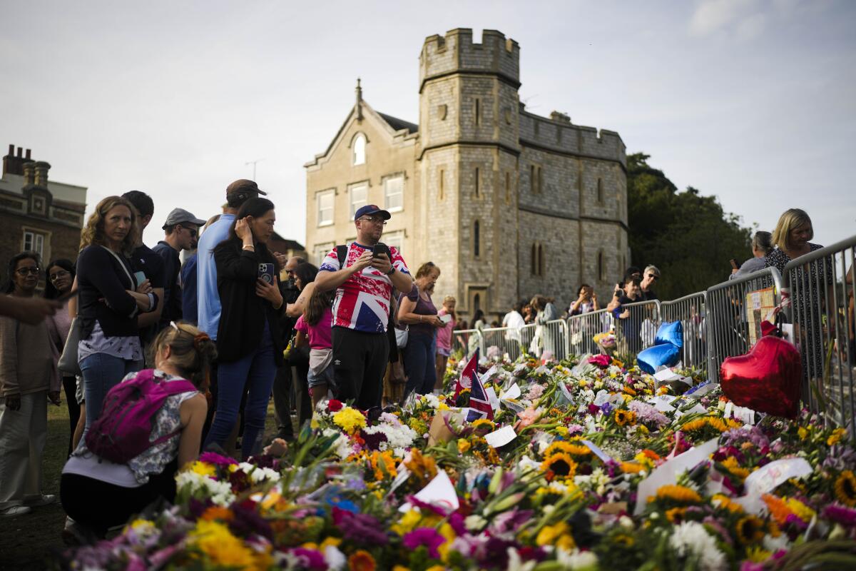 People gather at flowers and messages to tribute Queen Elizabeth II, in front of Windsor Castle in Windsor, England, Sunday, Sept. 11, 2022. Queen Elizabeth II, Britain's longest-reigning monarch and a rock of stability across much of a turbulent century, died Thursday Sept. 8, 2022, after 70 years on the throne. She was 96. (AP Photo/Markus Schreiber)