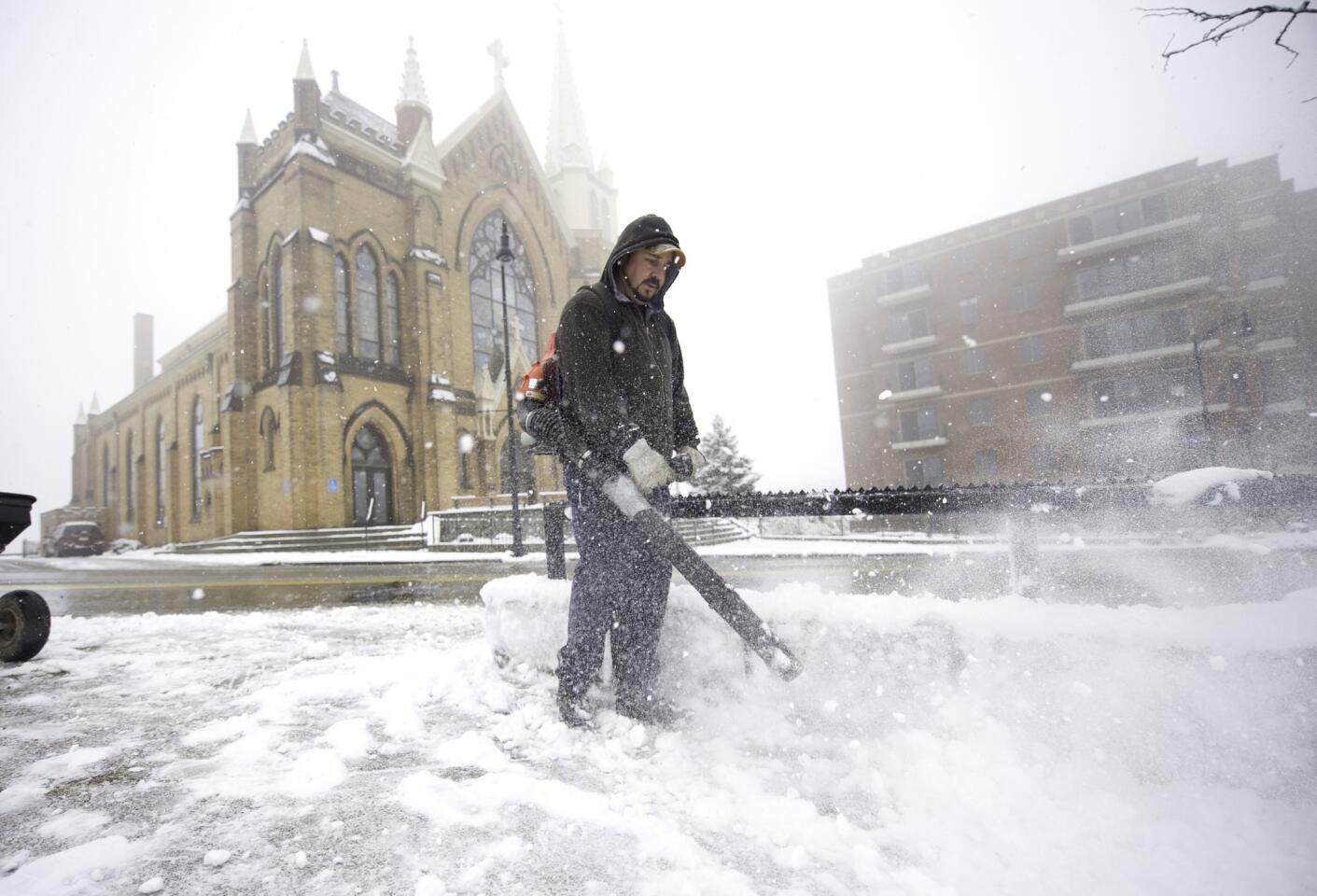 Mark Swigart uses a leaf blower to remove snow from the sidewalk along Grandview Avenue in Pittsburgh. Along the East Coast winter storms threatened to make Thanksgiving holiday travel dangerous.