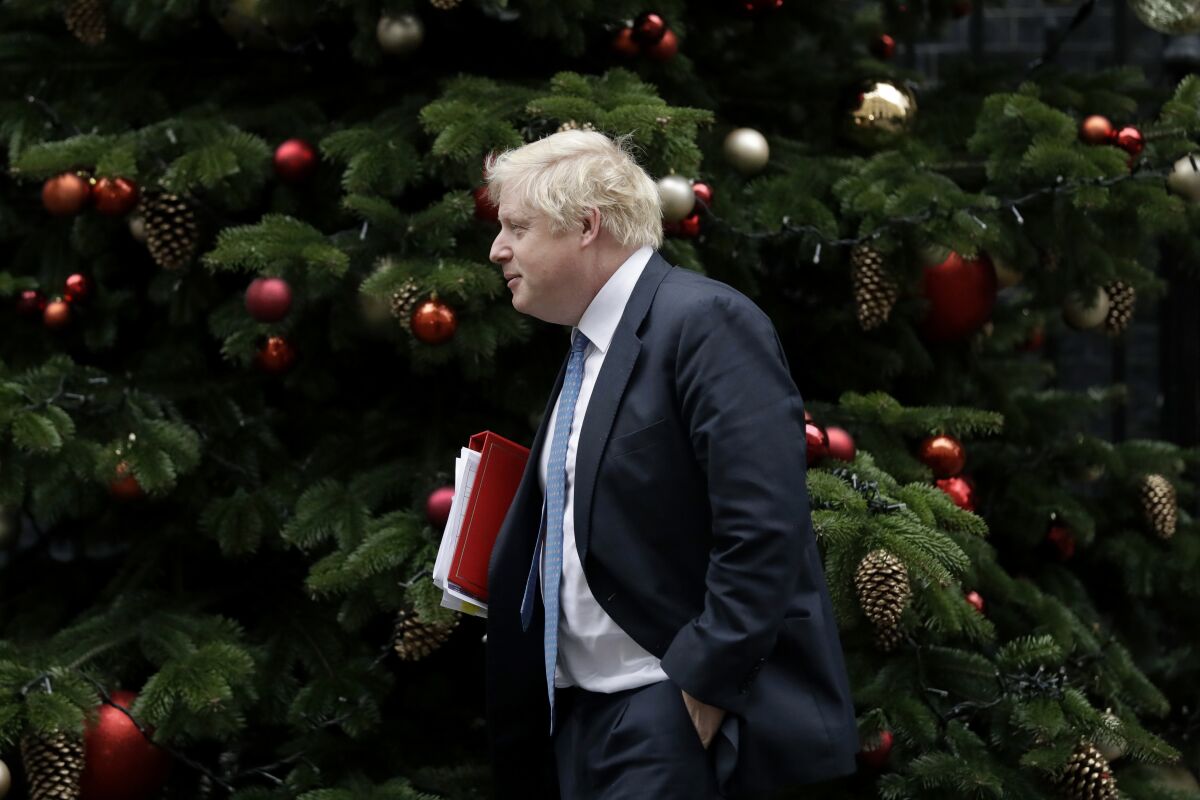Boris Johnson holds a binder and walks past a big Christmas tree.