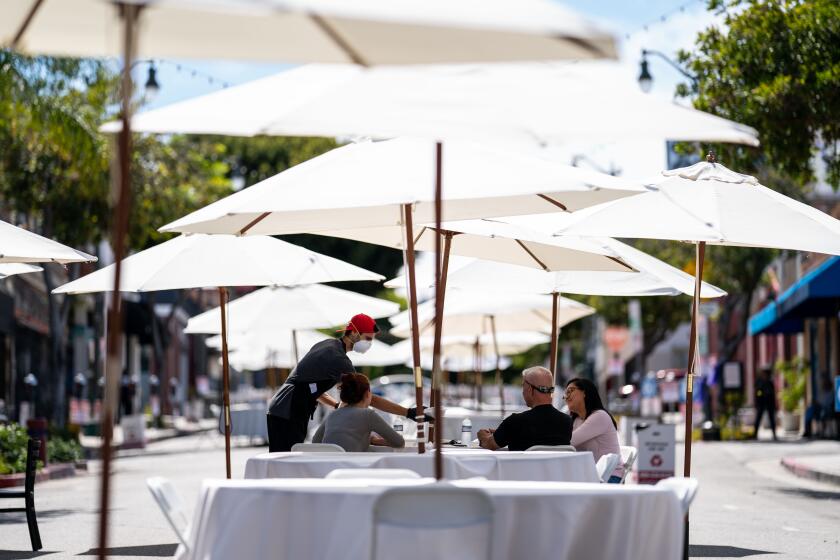 SAN PEDRO, CA - MAY 29: A worker from La Siciliana brings out food for people sitting at a table along a section of Sixth Street that is closed down between Mesa and and Centre streets in San Pedro where seating for dining is on Friday, May 29, 2020 in San Pedro, CA. On Friday, Los Angeles County received permission to reopen restaurants for in-person dining and resume services at barbershops and hair salons, marking a new phase in the regions efforts to restart the devastated retail economy. (Kent Nishimura / Los Angeles Times)