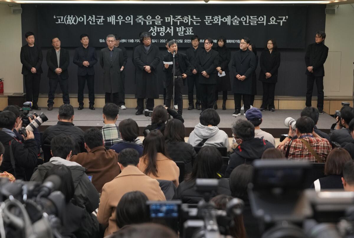 A line of people dressed in black standing onstage speaking to an audience 