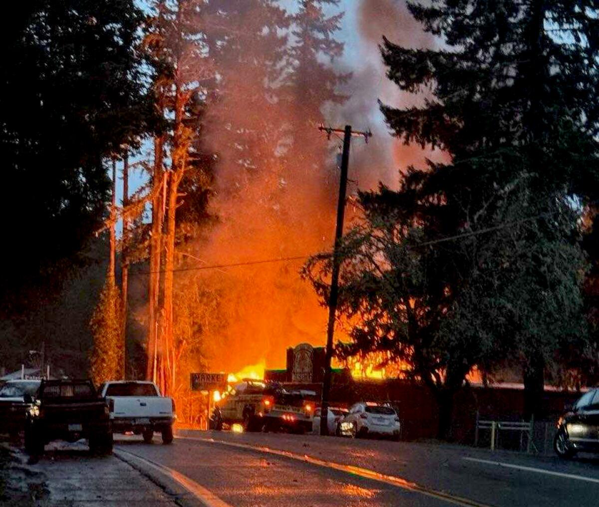 Flames cast an orange glow on a tree-lined rural street.