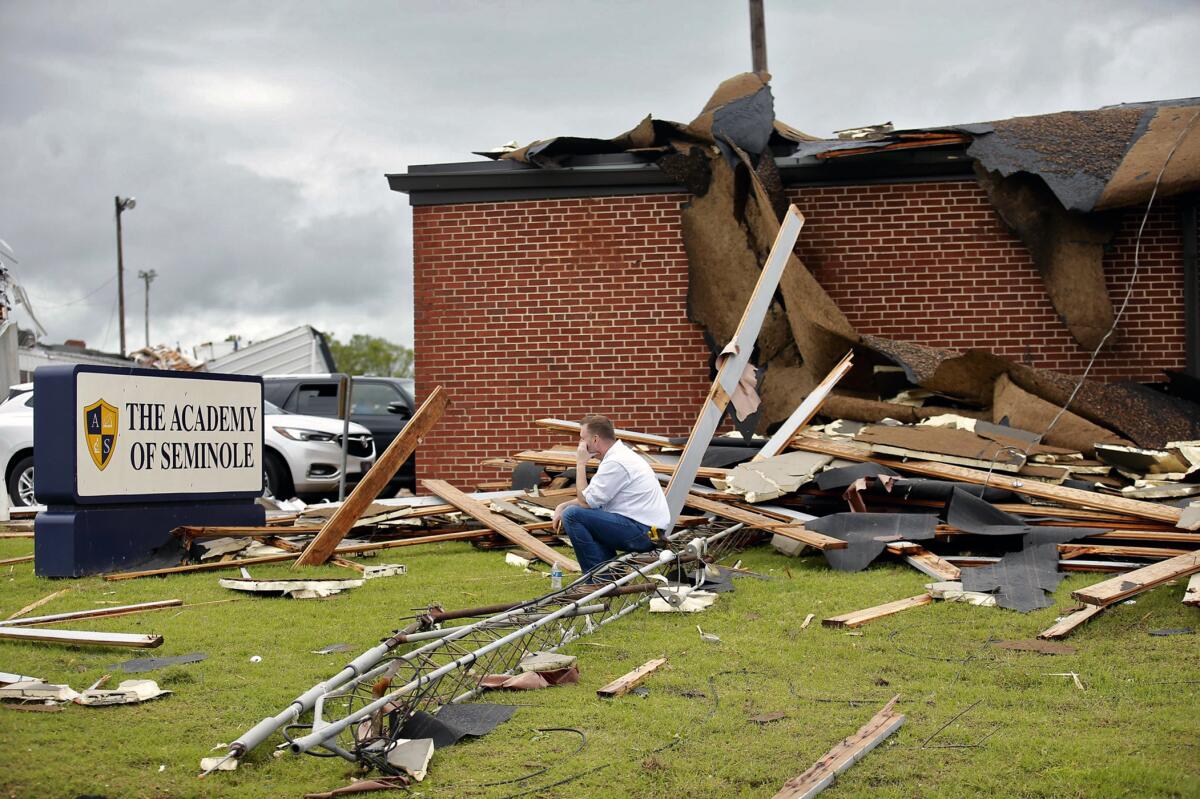 A man sits on the rubble of a damaged brick building