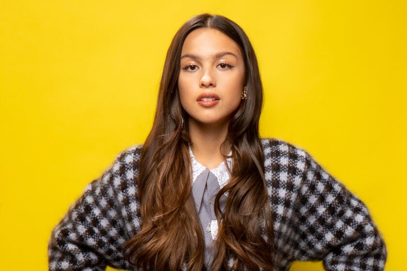 Olivia Rodrigo posing in a checkered sweater against a yellow background