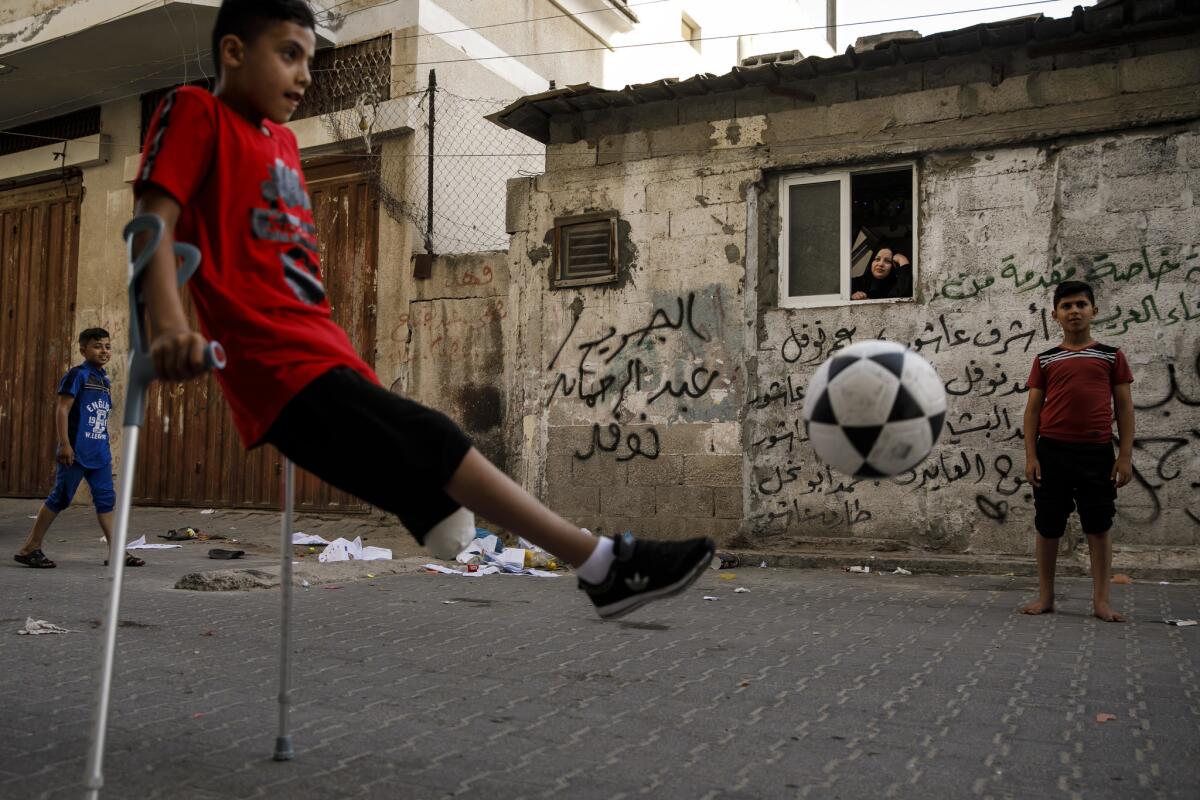Abdel-Rahman Nofal plays soccer outside his home in the Gaza Strip as his mother, Fatima, watches from a window.